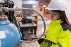 asiatischer ingenieur, der in der betriebshalle arbeitet, thailänder tragen helmarbeiten, er arbeitete mit fleiß und geduldig, sie überprüfte den ventilregler am wasserstofftank. foto