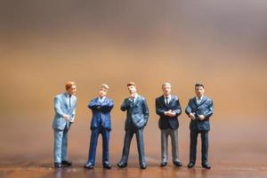 Miniaturgeschäftsleute, die auf einem hölzernen Hintergrund, Geschäftsleiter und Teamarbeitskonzept stehen foto