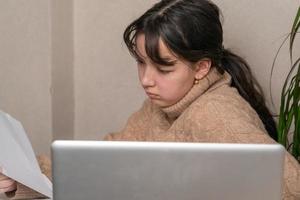 Mädchen arbeitet mit Dokumenten, die vor einem Laptop an ihrem Schreibtisch sitzen foto