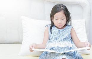 süß wenig asiatisch Mädchen im Nachthemd lesen ein Buch. foto