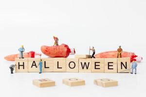 Miniaturarbeiter, die sich zusammenschließen, um Halloween-Party-Requisiten mit Holzklötzen mit dem Text Halloween auf einem weißen Hintergrund zu schaffen foto