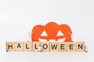 Miniaturarbeiter, die sich zusammenschließen, um Halloween-Party-Requisiten mit Holzklötzen mit dem Text Halloween auf einem weißen Hintergrund zu schaffen foto