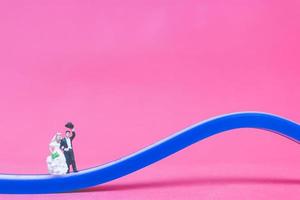 Miniaturhochzeit, eine Braut und ein Bräutigam auf einer Brücke auf einem rosa Hintergrund foto