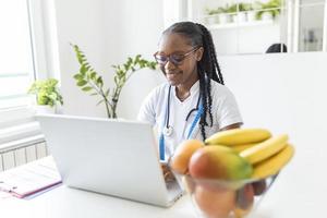 lächelnde ernährungsberaterin in ihrem büro zeigt sie gesundes gemüse und obst, gesundheits- und diätkonzept. weibliche ernährungsberaterin mit früchten, die an ihrem schreibtisch arbeitet. foto