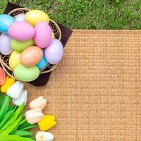 glücklich Ostern Urlaub Gruß Karte Konzept. bunt Ostern Eier und Frühling Blumen auf Papyrus Rattan weben Textur Hintergrund. eben legen, oben Sicht, Kopieren Raum. foto