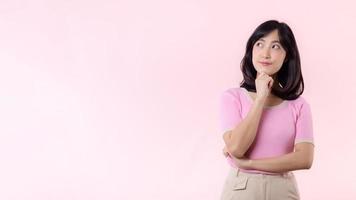 Porträt schön jung asiatisch Frau nachdenklich Denken ein Idee isoliert auf Rosa Pastell- Hintergrund. Teenager weiblich Person ziemlich Lächeln mit Denken Geste Konzept. foto