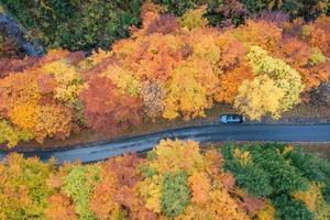 Antenne Aussicht von ein Auto Stehen auf das Seite von das Straße umgeben durch Herbst farbig Bäume foto
