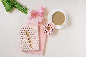 Frühling Blog Konzept. Tasse von Kaffee, Krapfen und Strauß von Rosa Tulpen auf Beige Hintergrund. eben legen, oben Aussicht feminin Schreibtisch. foto