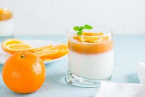 hausgemacht Panna Cotta mit Orange und Minze Blatt im ein Glas und ein ganze Orange auf ein Licht Tisch. Süss Italienisch Dessert