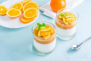 Orange Panna Cotta mit Minze Blatt im Brille und Orange Scheiben auf ein Teller auf ein Licht Tisch. Süss Italienisch Dessert foto