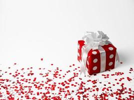 Geschenk zum Neu Jahr, Weihnachten, Geburtstag, geliebt Einsen. rot Polka Punkt Box mit Weiß Bogen auf Weiß Hintergrund mit Konfetti. foto