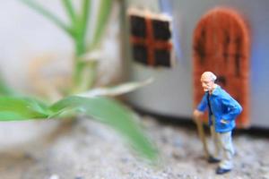 Miniatur Zahl von ein Großvater Wer ist warten im Vorderseite von das Haus. foto