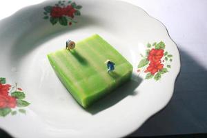 ein schließen oben von ein Miniatur Zahl von ein Farmer Wer ist Landwirtschaft auf ein Grün Schicht Kuchen mögen ein Reis Feld. Farmer Landwirtschaft Konzept. foto