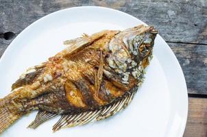 gebraten Fisch Tilapia auf Weiß Gericht auf hölzern Hintergrund, thailändisch Essen Stil foto