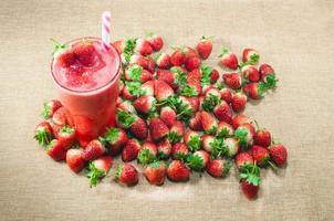 erdbeersaft-smoothie im glas mit frischer erdbeere auf traditionellem sacktextilhintergrund. sommer erfrischendes gesundes getränk foto