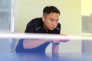 Mann, der Tischtennis mit Schläger und Ball in einer Sporthalle spielt foto