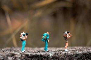 Miniatur-Rucksacktouristen, die auf einem Betonboden mit einem Bokeh-Naturhintergrund stehen foto