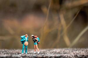 Miniatur-Rucksacktouristen, die auf einem Betonboden mit einem Bokeh-Naturhintergrund stehen foto