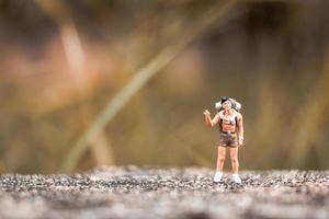 Miniatur-Rucksacktourist, der auf einem Betonboden mit einem Bokeh-Naturhintergrund steht foto