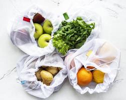 Obst und Sommergemüse in wiederverwendbaren umweltfreundlichen Netzbeuteln auf Marmorhintergrund foto