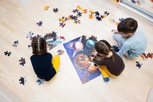 Kinder verbinden Puzzleteile in einem Kinderzimmer im Erdgeschoss zu Hause. lustige familienaktivität freizeit. foto