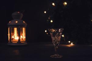 Glas mit Weiß Wein mit Girlande Beleuchtung und Kerze Laterne auf das Hintergrund. dunkel Bild. Verbrennung Kerze. golden Getränk im das Glas. schön Beleuchtung reflektiert im das Glas. foto