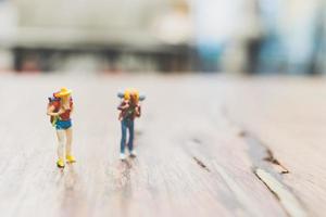 Miniatur-Rucksacktouristen-Touristen, die auf einem hölzernen unscharfen Hintergrund stehen foto