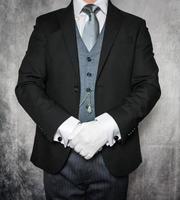 Porträt eines Butlers oder Hotelportiers in dunklem Anzug und weißen Handschuhen, die begierig darauf sind, Ihnen behilflich zu sein. Konzept eleganter Gastfreundschaft und professioneller Höflichkeit. foto