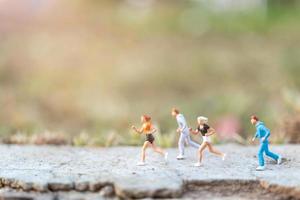 Miniaturmenschen, die auf einer Straße mit einem Naturhintergrund-, Gesundheits- und Lebensstilkonzept laufen foto