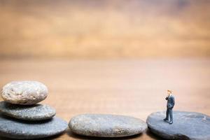 Miniaturgeschäftsmann, der auf einem Stein steht, fordert und riskiert Konzept foto