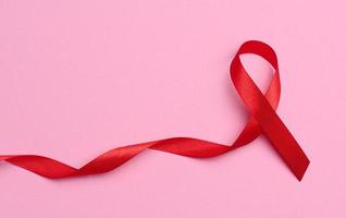 ein Seide rot Band im das bilden von ein Bogen auf ein Rosa Hintergrund, ein Symbol von das Kampf gegen AIDS und ein Zeichen von Solidarität und Unterstützung foto