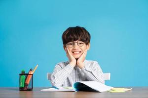 Porträt von Schule Junge Sitzung und studieren auf ein Blau Hintergrund foto