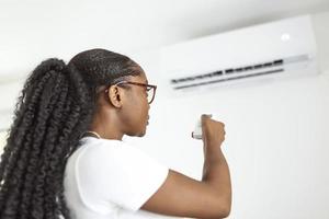 glücklich jung Frau halten Fernbedienung Steuerung entspannend unter das Luft Conditioner foto