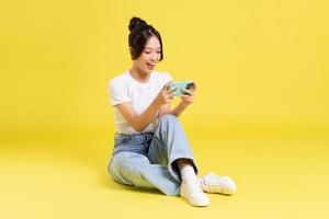 Porträt von ein schön jung asiatisch Mädchen Sitzung auf ein Gelb Hintergrund foto