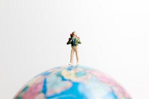 Miniaturperson, die auf einem Globus mit einem weißen Hintergrund, Reisekonzept steht foto