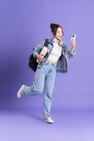 Porträt von ein schön asiatisch Schülerin tragen ein Rucksack auf ein lila Hintergrund foto