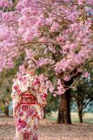 asiatisch Dame im traditionell Kimono Kleid genießen Reise und halten Dango in der Nähe von Kirsche blühen Baum im Frühling Festival. Emotion Lächeln foto