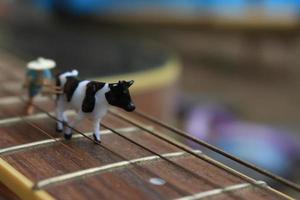 Miniatur Zahl von ein Farmer Pflügen ein Feld mit seine Kuh auf ein Gitarre. foto