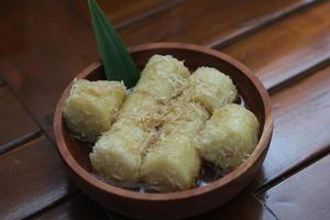 ein schließen oben von Lupis mit gerieben Kokosnuss und braun Zucker Soße serviert im ein hölzern Schüssel. indonesisch traditionell Essen Foto Konzept.