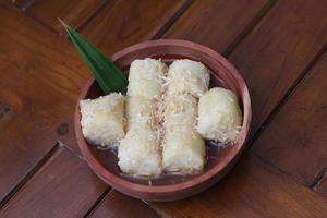 ein schließen oben von Lupis mit gerieben Kokosnuss und braun Zucker Soße serviert im ein hölzern Schüssel. indonesisch traditionell Essen Foto Konzept.
