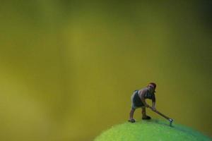 Miniatur Zahl von ein weiblich Farmer Arbeiten das Land mit ein Sonnenaufgang Hintergrund. foto