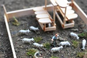 ein schließen oben von Miniatur Zahl von ein Ziege Hirte Fütterung im ein hölzern Käfig. Schäfer Konzept. foto