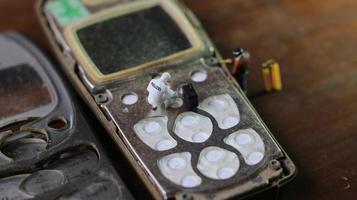 Miniatur Zahl von ein Techniker reparieren ein alt gebrochen Zelle Telefon. Arbeiten Techniker Konzept. foto