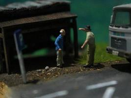 ein schließen oben von ein Miniatur Zahl von ein alt Mann reden zu andere Menschen im ein alt Gebäude durch das Seite von das Straße. foto