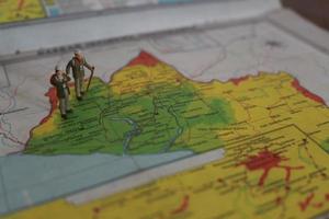 Miniatur Zahl von ein Forscher posieren auf ein Karte oder Atlas foto