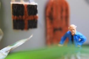 Miniatur Zahl von ein Großvater Wer ist warten im Vorderseite von das Haus. foto