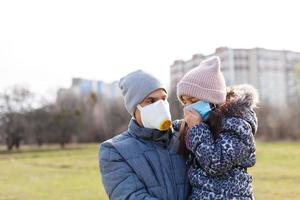 Vater und Tochter sind herzlich gekleidet im kalt Wetter und tragen schützend medizinisch Masken auf ihr Gesichter während ein Grippe Epidemie oder Luft Verschmutzung. ein Mann und ein Kind auf ein Stadt Straße foto
