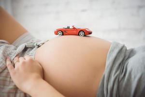 Mittelteil der schwangeren Frau mit Spielzeugmaschine foto