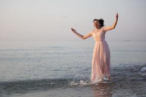 glücklich mittleren Alters Frau im ein Kleid spritzt Wasser durch das Meer. foto