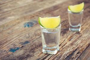 Wodka und Limette Scheiben auf hölzern Hintergrund. foto